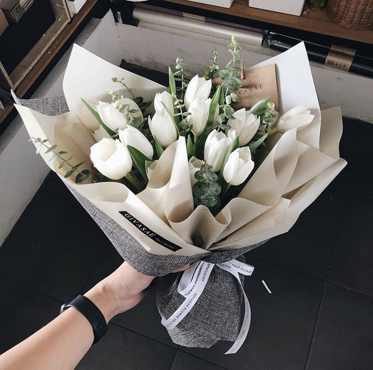 a bouquet of white tulips is being held by a woman's hand