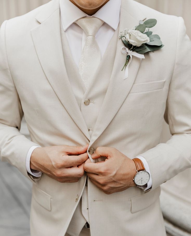 a man in a white suit and flower boutonniere with his hands on his chest