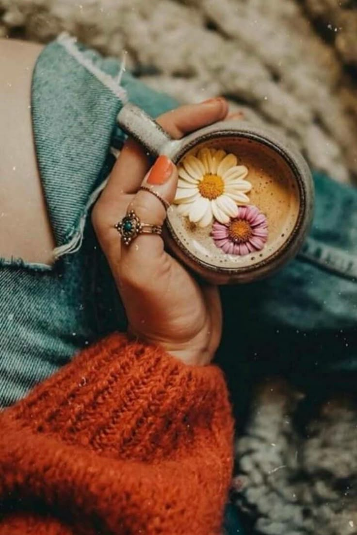 a woman is holding a cup with flowers in it and she has her hand on the mug