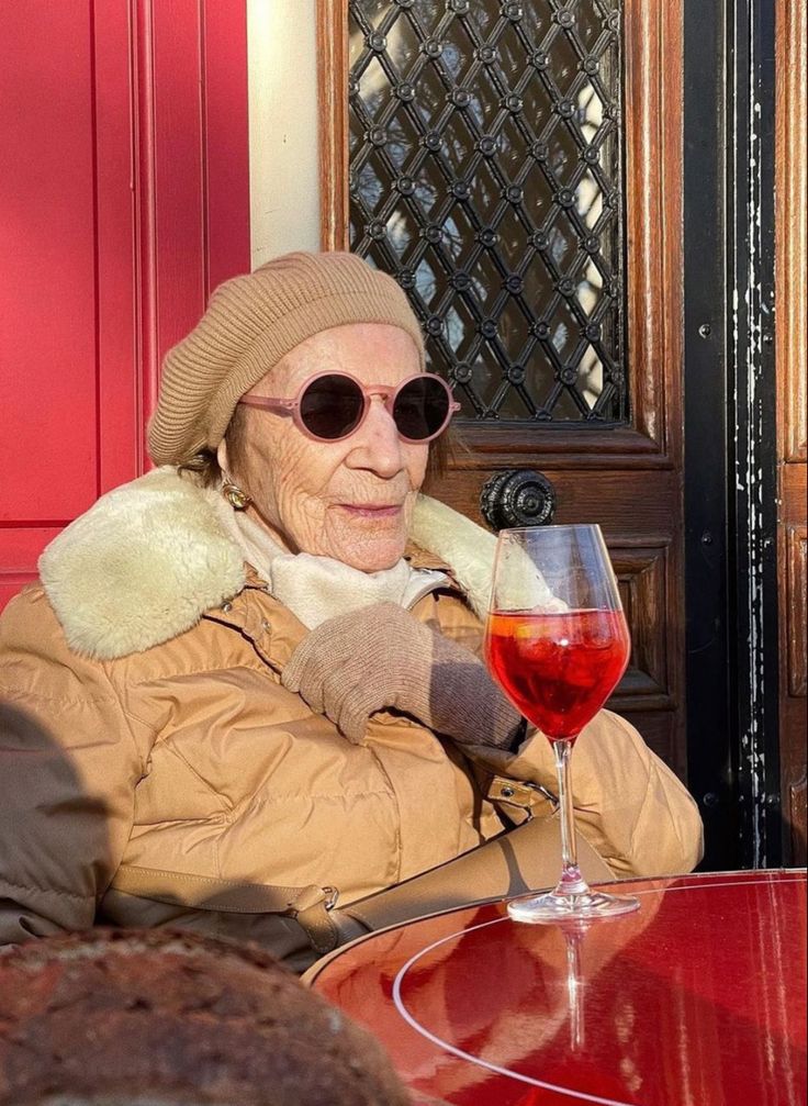 an old woman sitting at a table with a glass of wine