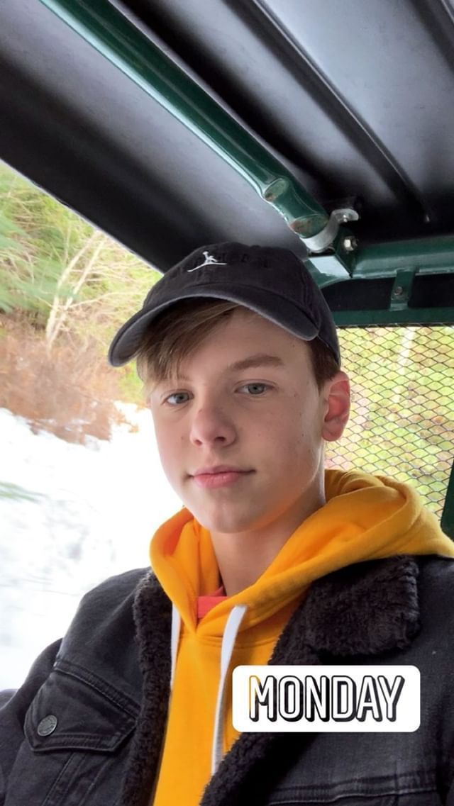 a young boy wearing a black hat and yellow scarf is sitting in the back of a vehicle