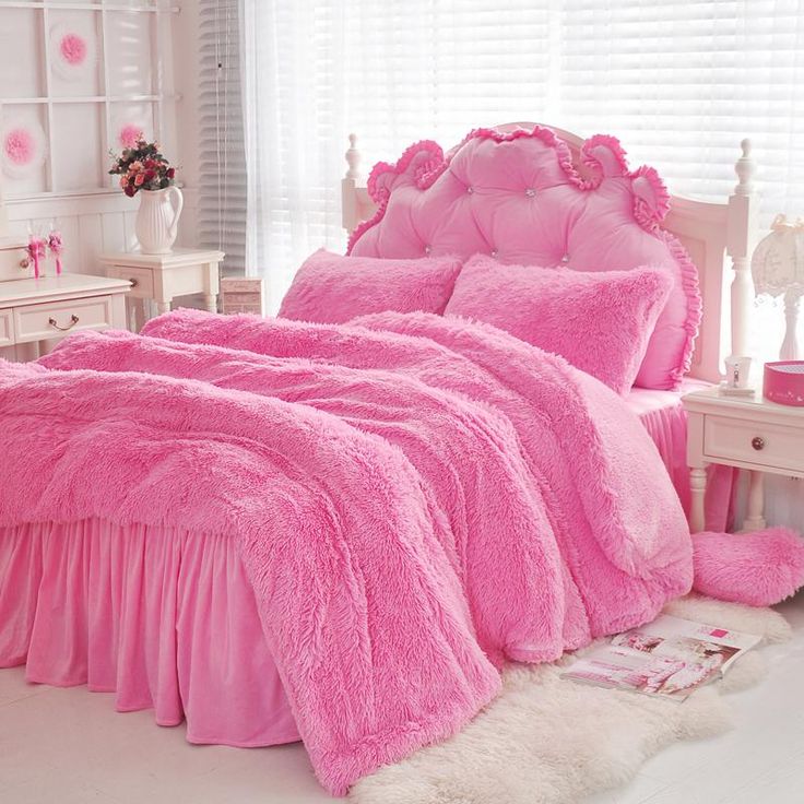 a bed with pink comforters and pillows in a white room next to a window