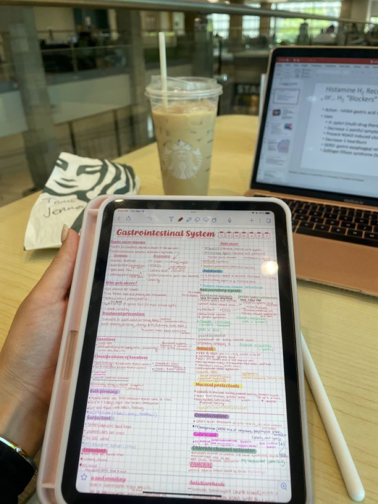 a person holding an electronic device in front of a laptop computer on a table with a cup of coffee