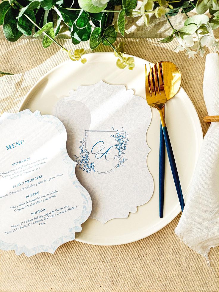 a white plate topped with a menu next to a gold fork and knife on top of a table