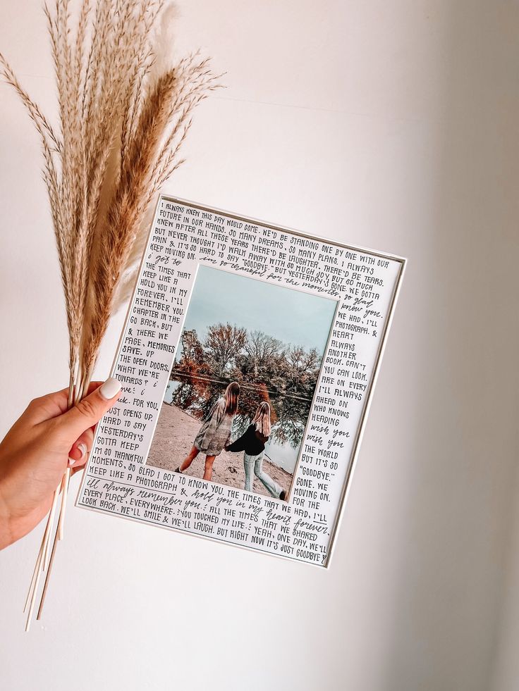 a person holding up an old book with a photo on it and some dried grass