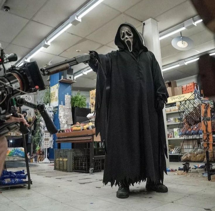 a man in a black robe and mask standing next to a camera on a tripod