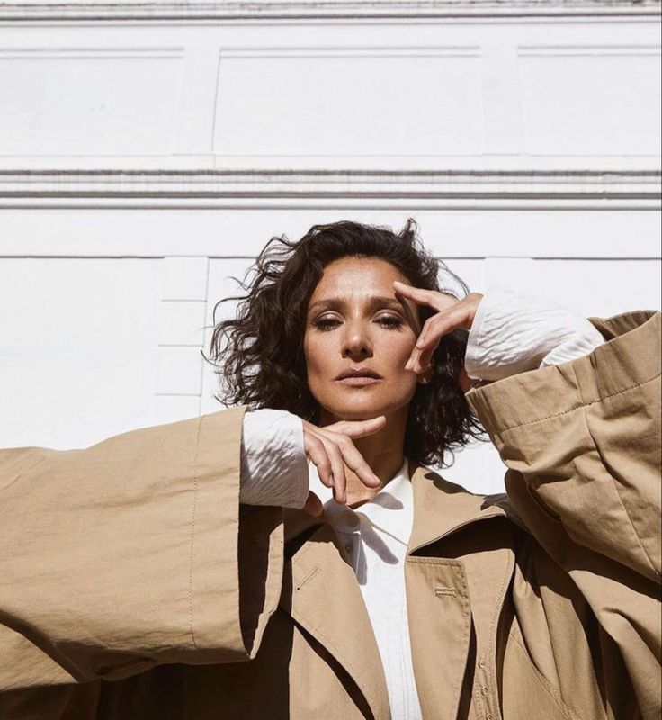 a woman in a trench coat is posing for the camera with her hands on her head