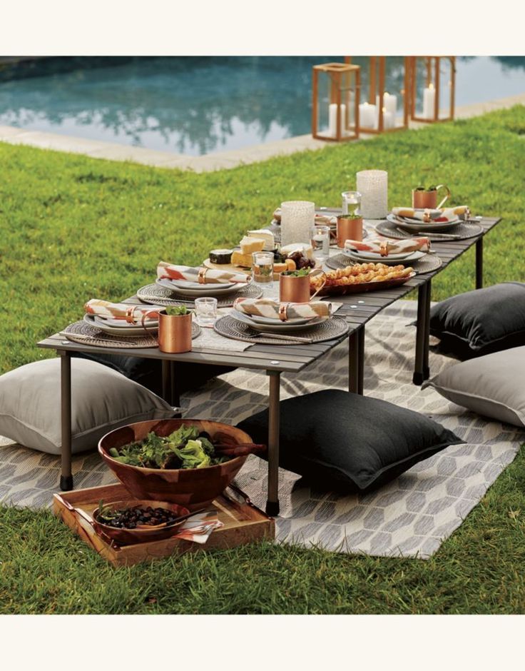 an outdoor table set up with food and drinks near a swimming pool in the background