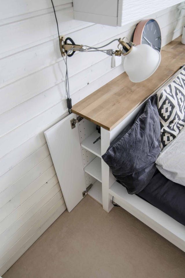 a bed with a wooden headboard next to a white wall and a lamp on top of it