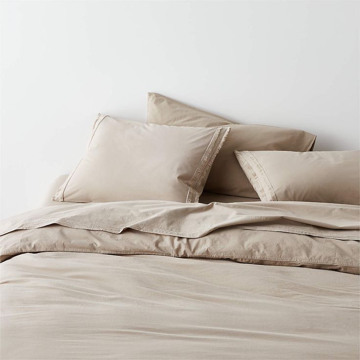 an unmade bed with beige sheets and pillows