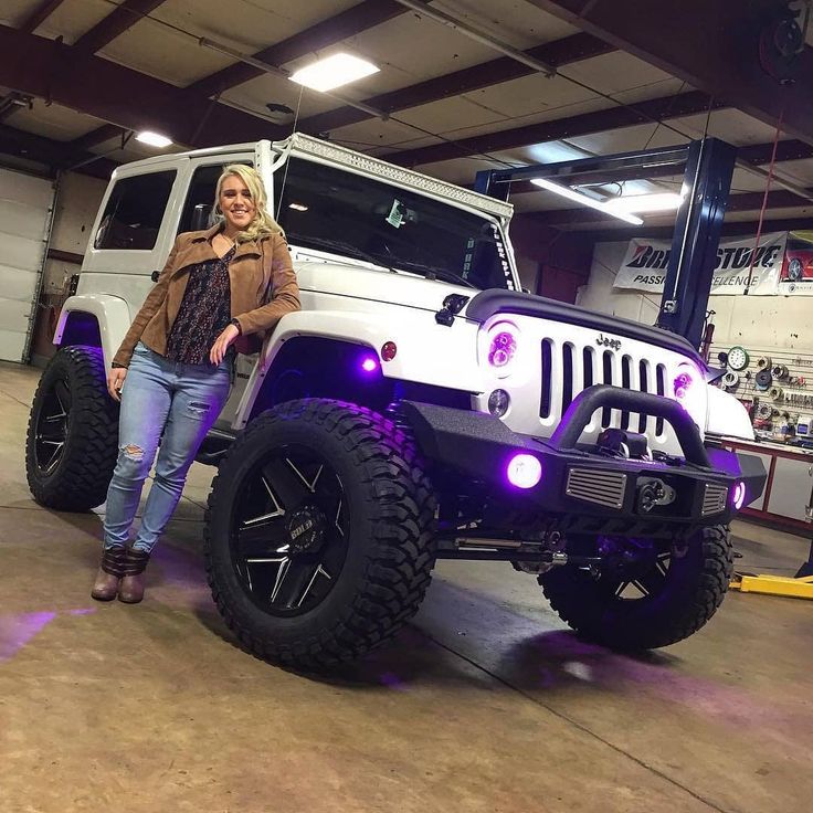 a woman standing next to a white jeep with purple lights on it's hood