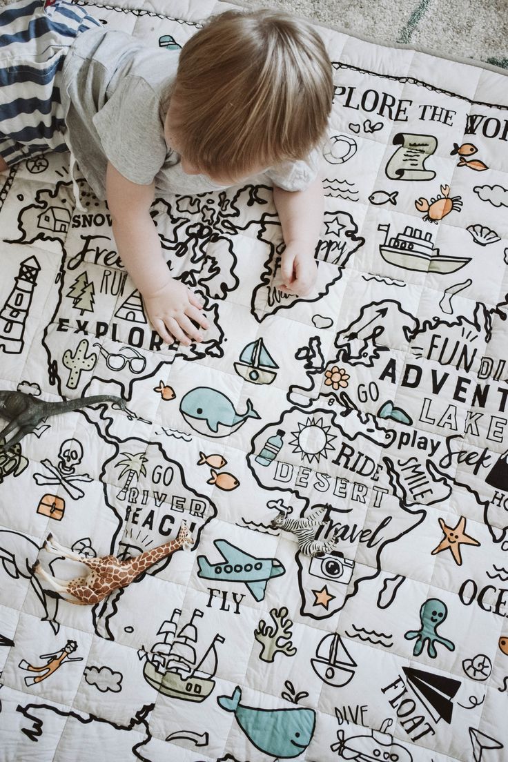 a young child is playing on a map quilt with animals and words all over it