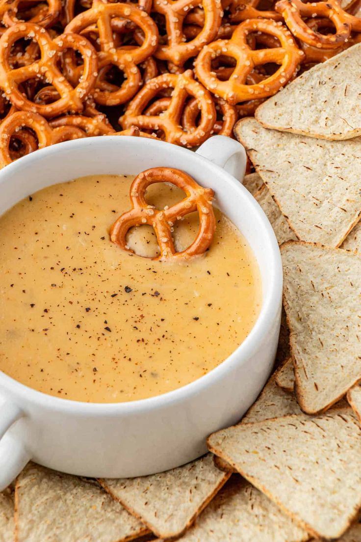 a white bowl filled with dip surrounded by crackers and pretzels on the side