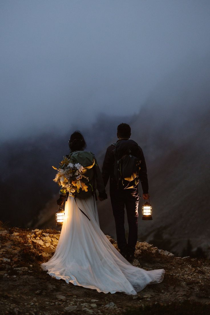 a bride and groom holding hands while walking up a hill in the mountains at night