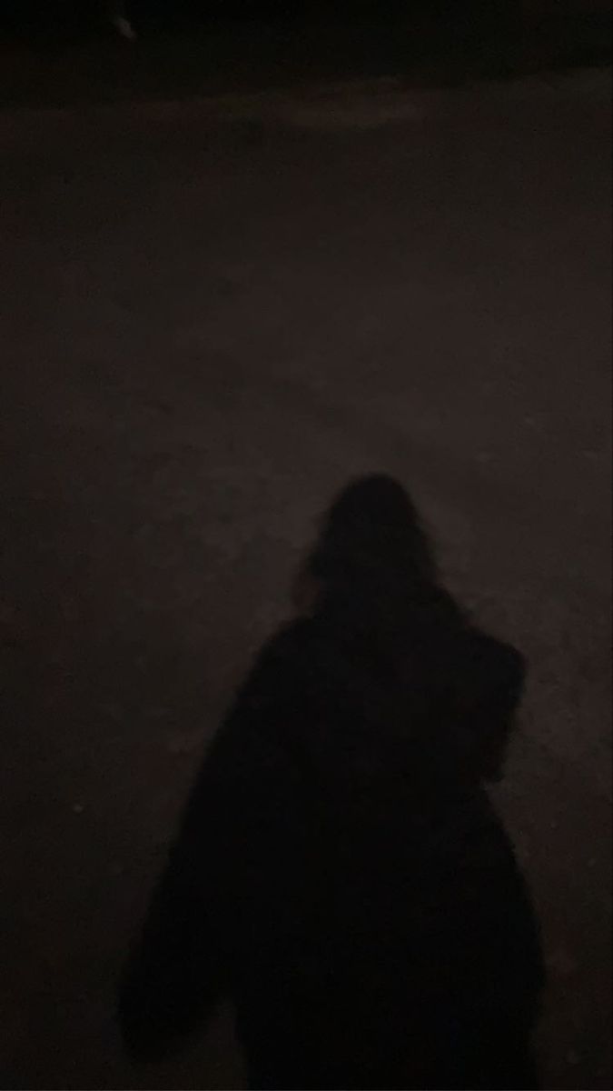 a person standing in the dark with their shadow on the ground and one hand up