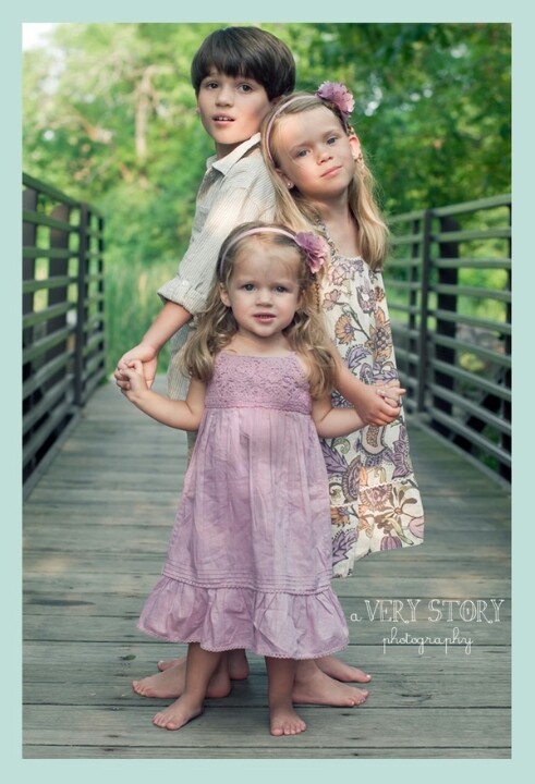 three children are standing on a wooden bridge