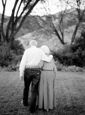 an older couple standing in the grass with their arms around each other's shoulders