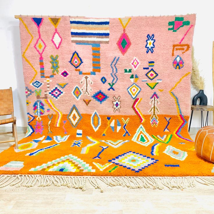 an orange rug with colorful designs and fringes on the floor next to a chair