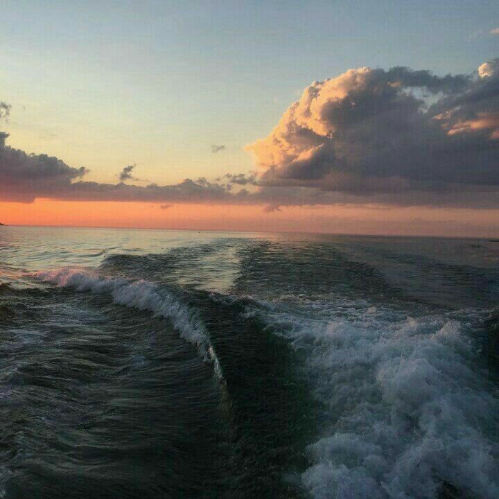 the sun is setting over the ocean as waves crash on the shore and clouds in the sky