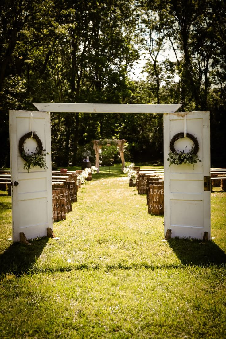 an outdoor ceremony setup with white doors and wreaths on each door, surrounded by grass