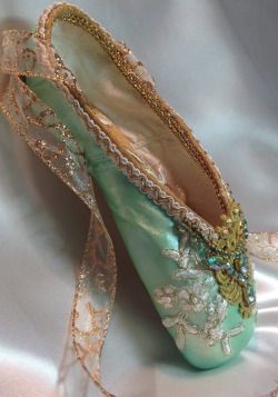 a pair of green ballet shoes with gold trimmings sitting on a satin surface