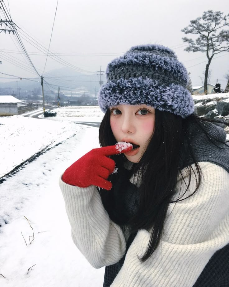 a young woman in winter clothes is holding something up to her mouth