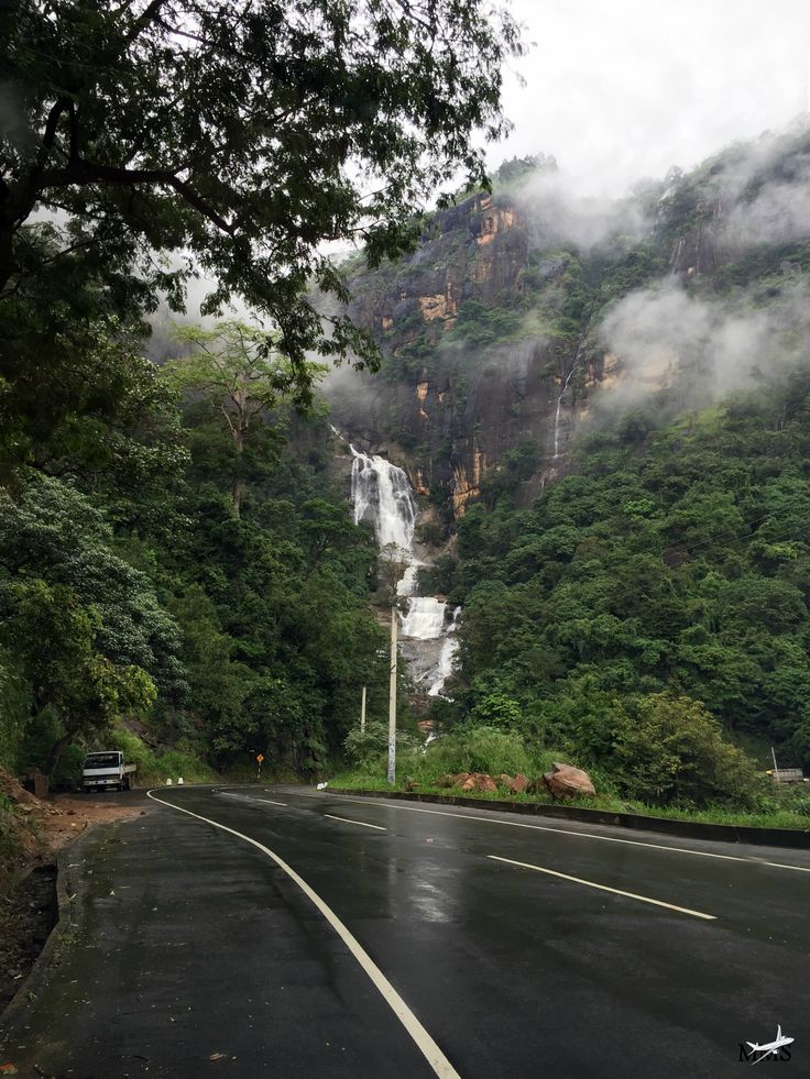 a car driving down the road in front of a waterfall on a cloudy day with fog