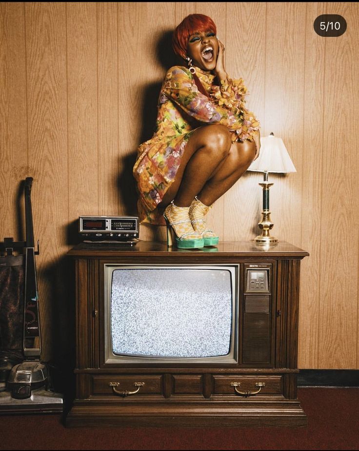 a woman sitting on top of a tv next to a lamp and a wooden wall