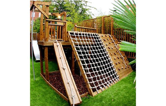 a wooden play set with a slide and climbing frame in the grass next to a palm tree