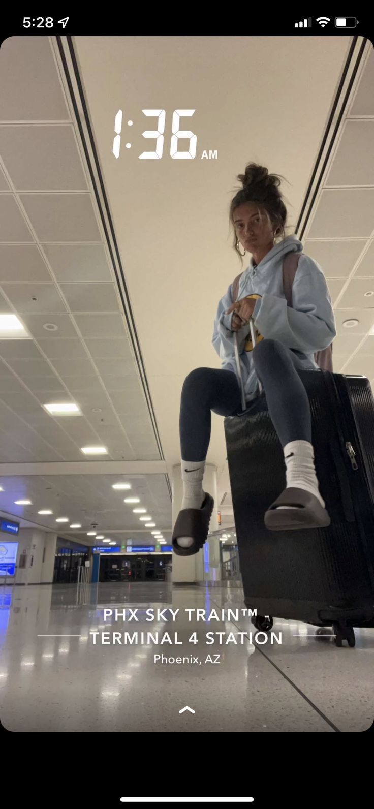 a woman sitting on top of a piece of luggage in an airport with her feet up