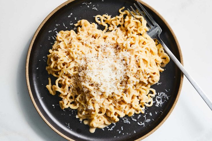 a black plate topped with pasta and parmesan cheese