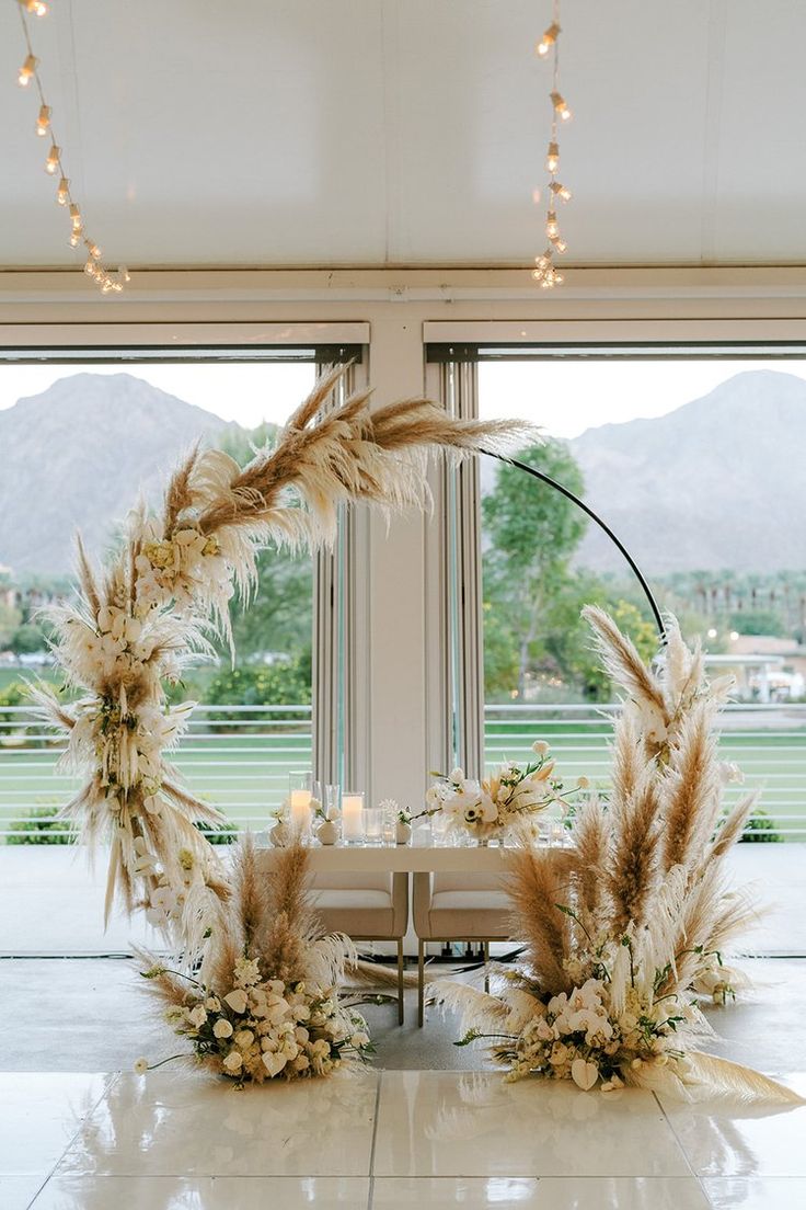 a table set up with flowers and candles in front of large windows