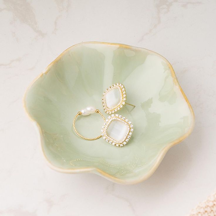 two rings sitting on top of a green flower shaped bowl with pearls in the middle