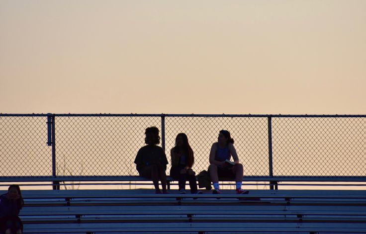 three people sitting on bleachers watching the sun set