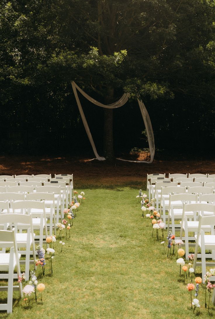 rows of white chairs are lined up in the grass for an outdoor ceremony with flowers on them