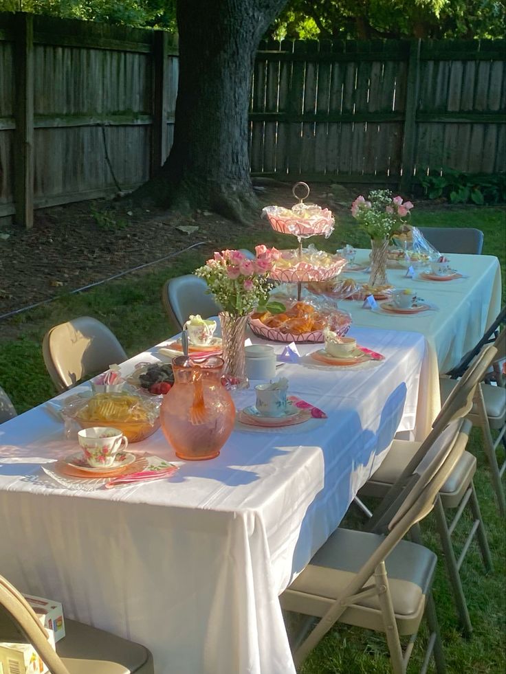 a table set up with flowers and tea cups on it in the back yard for an afternoon tea party