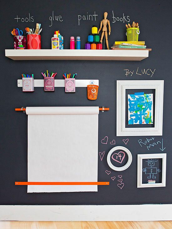 a black wall with white shelves and chalk writing on it, above the shelf is an image of children's artwork