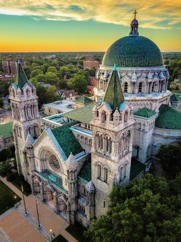 an aerial view of a cathedral with green roof and steeples in the city at sunset