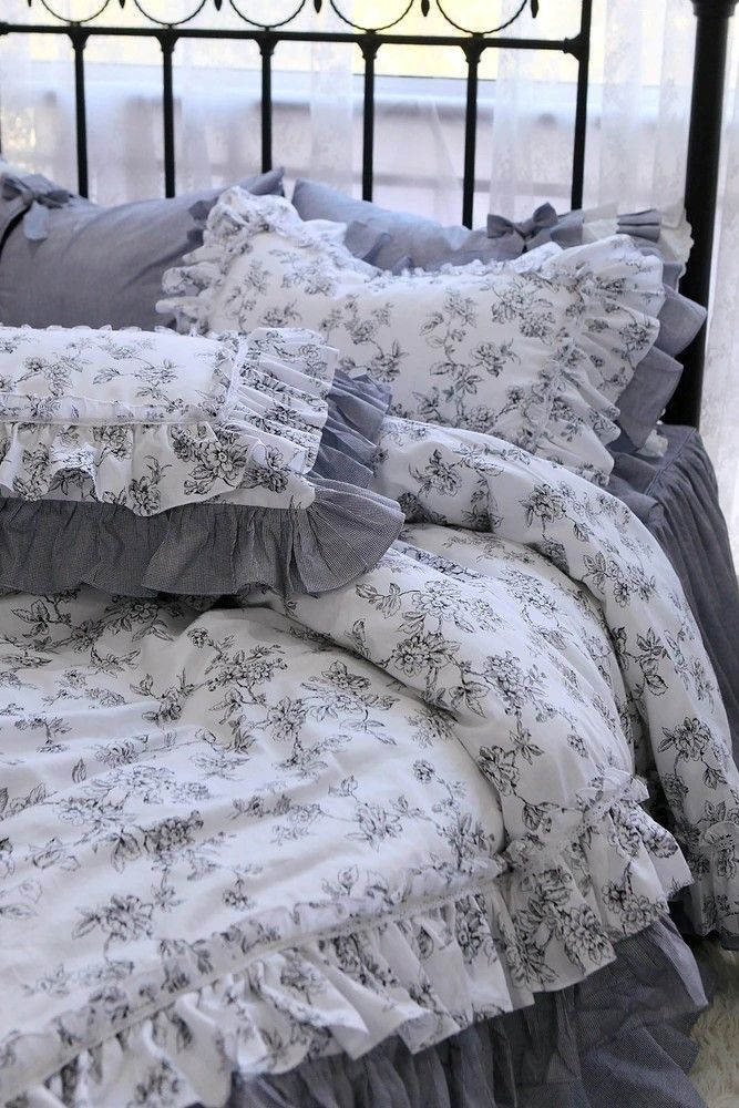 a bed with ruffled bedspread and pillows in front of a wrought iron headboard