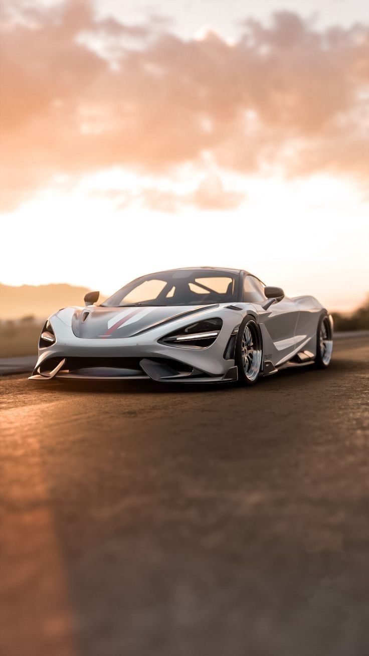 a silver sports car driving down a road under a cloudy sky in the sun set