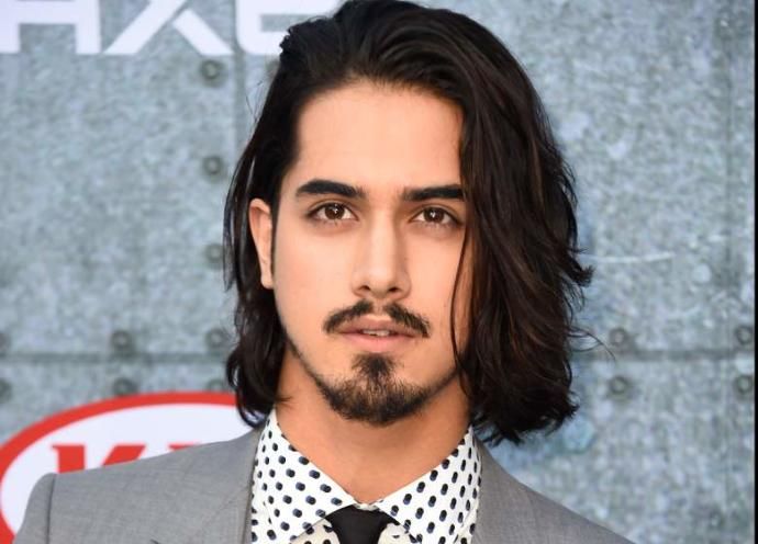 a man with long black hair and a beard wearing a gray suit, polka dot tie