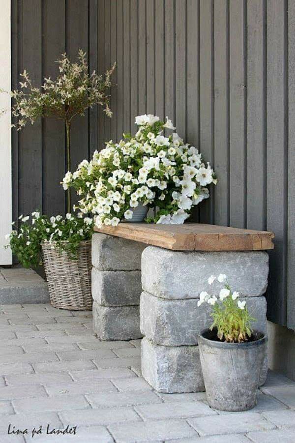 some white flowers are sitting in pots on the side of a building next to a bench