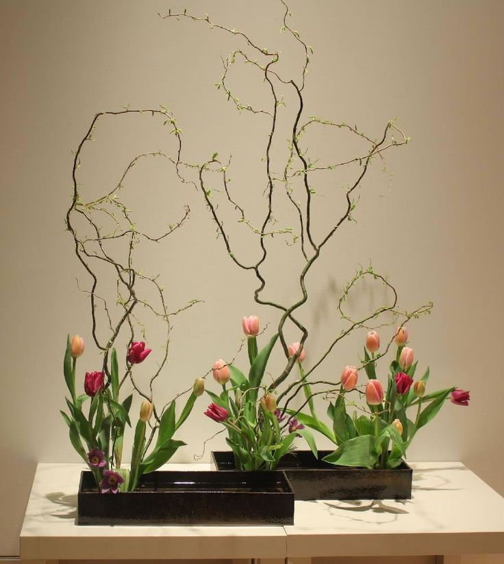 two black planters with flowers in them on a white countertop next to a wall