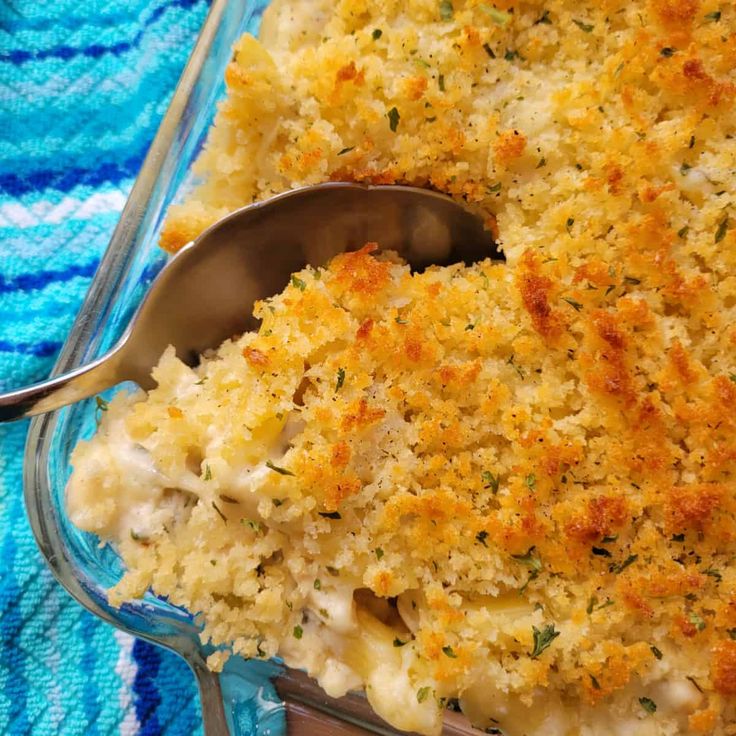 a casserole dish with chicken and cheese in it on a blue towel next to a spoon