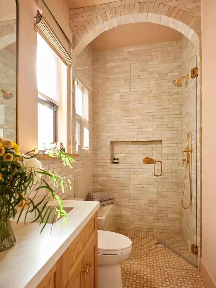 a white toilet sitting in a bathroom next to a shower and sink with a vase of flowers on the counter