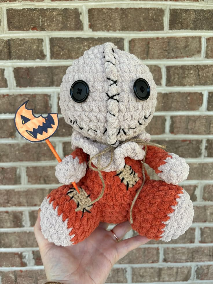 a hand holding a small crocheted stuffed animal in front of a brick wall