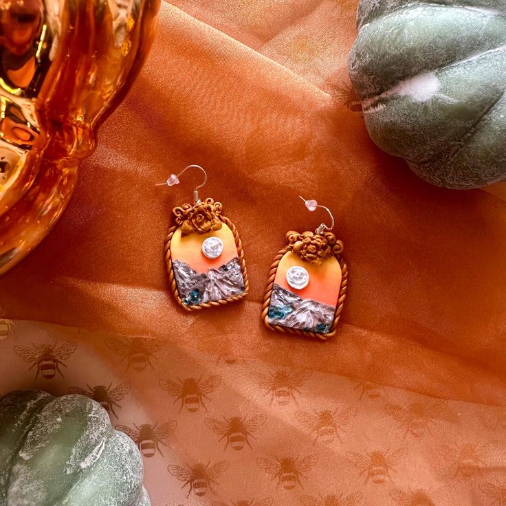 A pair of handmade arch-shaped earrings with a hand-sculpted golden frame and a mountain sunset landscape. Earring bases are silver, apply as dangles, and are nickel free and hypoallergenic. (Please read shop policies before purchasing). Polymer Clay Landscape, Clay Landscape, Mountain Sunset Landscapes, Golden Frame, Mountain Sunset, Sunset Landscape, Jewelry Inspo, Shop Policies, Clay Earrings