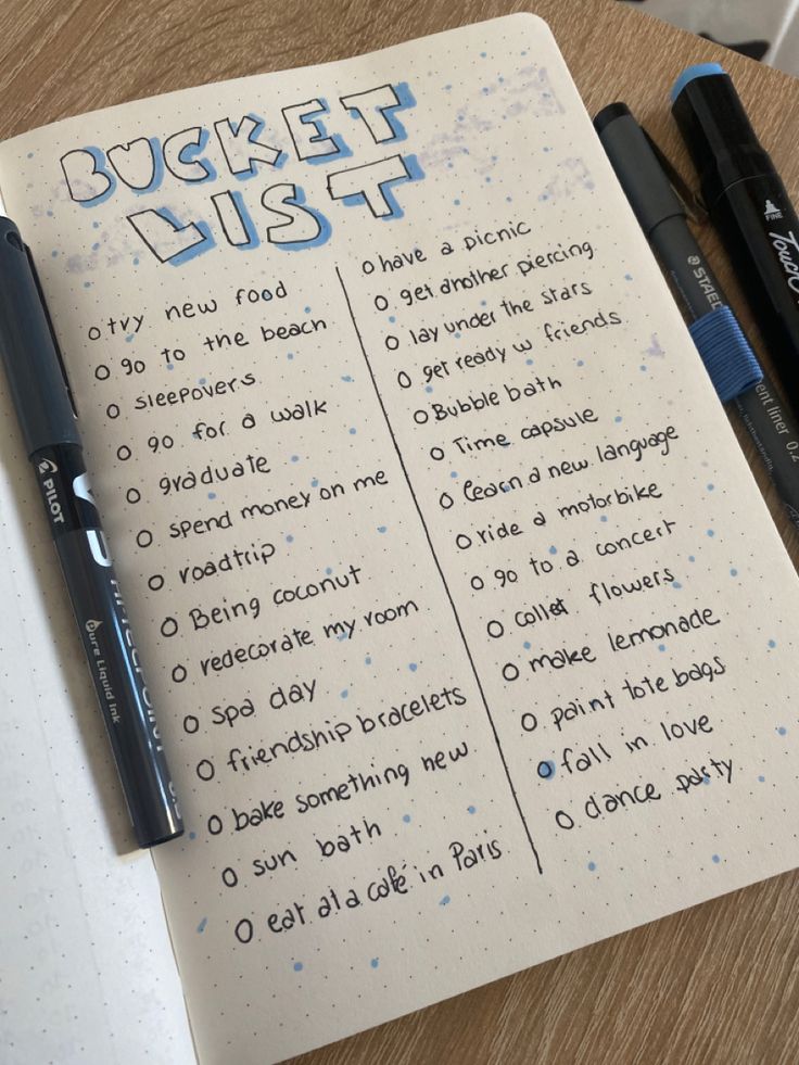 an open notebook with writing on it and two pens next to it, sitting on top of a wooden table