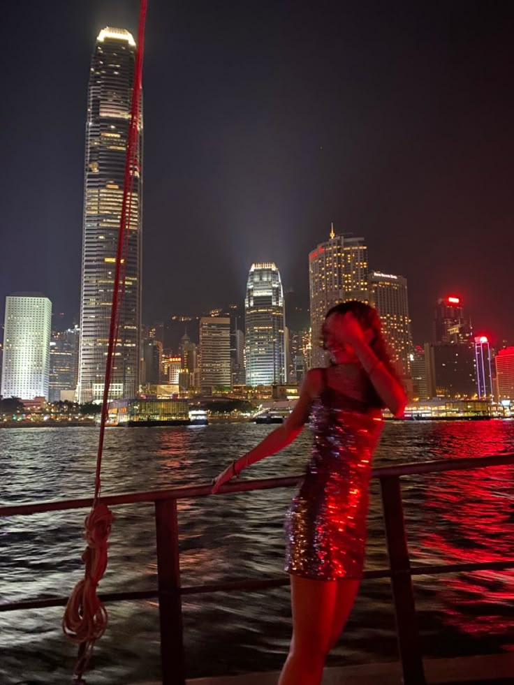 a woman standing on the side of a boat in front of a city skyline at night