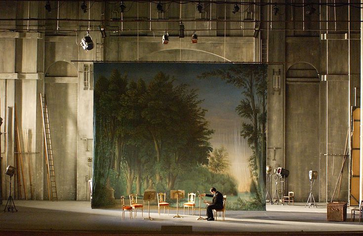 a man standing in front of a painting on a wall next to chairs and ladders